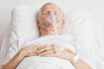 Close up of sick senior man lying in hospital bed with focus on IV drip needle in hand, copy space