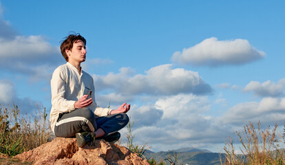 A Caucasian man from Spain sitting on a rock and meditating in grassy and disconnected area