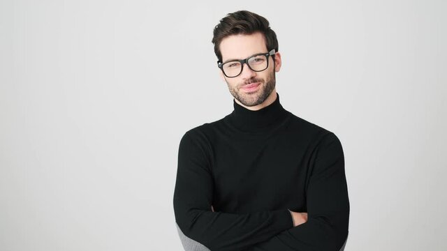 A handsome man is standing in a confident pose isolated over a white wall in a studio