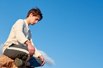 A dutch angle shot of a Caucasian man from Spain meditating on a rock on cloudy sky background