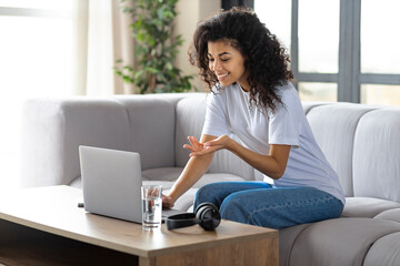 Beautiful young African American woman working with a laptop or receiving online education or training while sitting on the couch at home. Technology, remote work concept