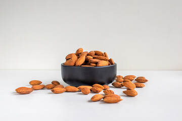 Almonds in a black bown on white tabel background.