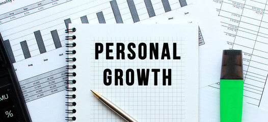 Text PERSONAL GROWTH on the page of a notepad lying on financial charts on the office desk.