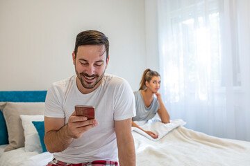 Obraz premium Young woman getting bored in the background while man using phone in the background. Beautiful young woman feeling annoyed as man texting on phone. 