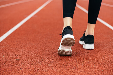 Young athletic girl legs runner prepares for a productive fitness workout marathon on running track treadmill. Female sporty model dressed sportwear on the city stadium. Image with copy space