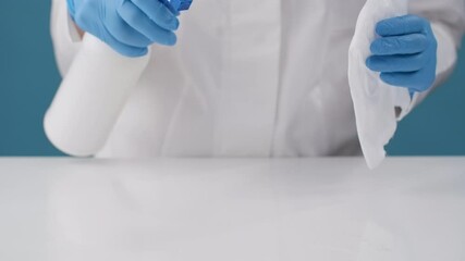 A nurse in a white coat sprays and wipes an antiseptic solution onto an infectious surface after an infected sick patient.