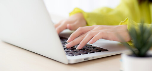 Closeup of hand young asian businesswoman working on laptop computer on desk at home office, freelance looking and typing on notebook on table, woman studying online, business and education concept. © NT_studio