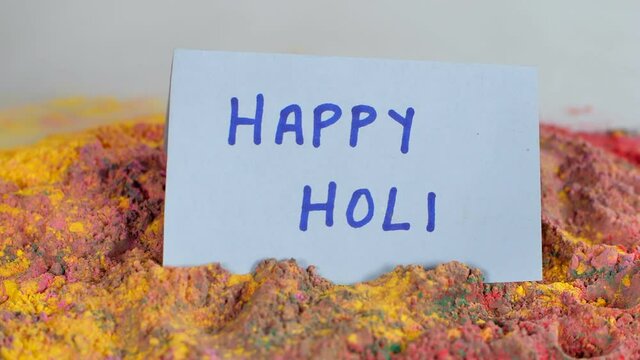 Handmade greeting card to wish Holi dropping on mixed Gulal (Holi colors). Popular Indian spring festival celebrated with colors - Dry organic multicolor Abeer against a white background