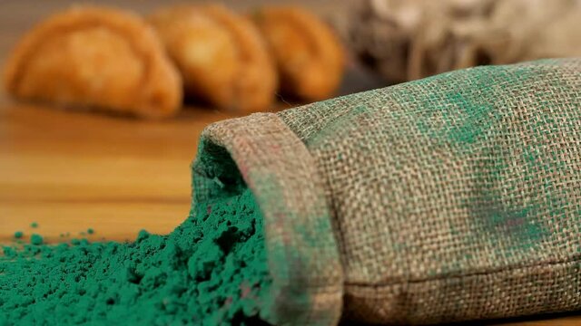 A sack of dark green naturally made Gulal dropping on a wooden surface. Traditional sweets and Abeer for the celebration of Holi festival - popular Indian spring festival of colors