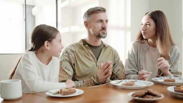 A positive soldier man is talking to this family while eating breakfast after returning from military service sitting in the white kitchen at home