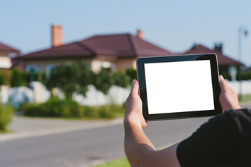A tablet in the hands of a man, against the backdrop of a house.