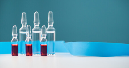 A row of glass ampoules on a blue background stand on a white table with a tourniquet for intravenous injections. Horizontal, copy space.
