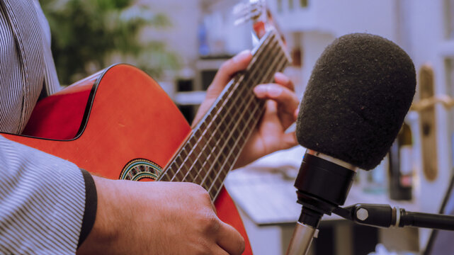 HANDS OF AN artist holding classical guitar in front of a recording microphone