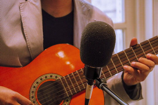 HANDS OF AN artist holding classical guitar in front of a recording microphone