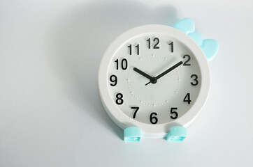 A white clock with a blue bow lies on a white table.