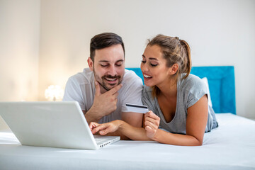 Fototapeta premium Young couple is browsing the internet on a laptop. Couple is shopping online using laptop and credit card in the bed. Beautiful young amorous couple using laptop, on bed.