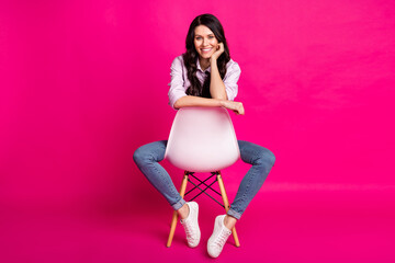 Full size photo of optimistic brunette nice lady sit wear jacket jeans sneakers isolated on pink color background