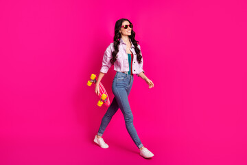Full size profile side photo of young beautiful cool confident girl go walk with skateboard isolated on pink color background