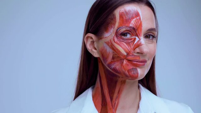 Young woman with half of face with muscles structure under skin. Model for medical training on a light background. Close up video of face human anantomy.