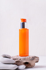 Orange dispenser bottle on stone against the beige background. Skincare product presentation
