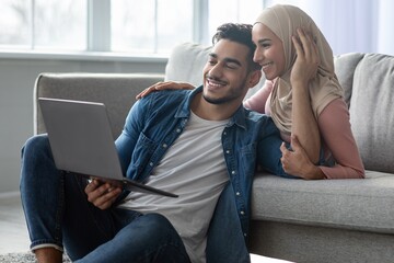 Loving young arab man and woman using laptop at home