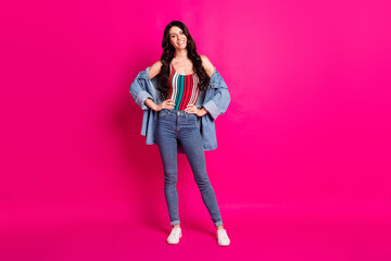 Full length photo of charming adorable young lady dressed jeans jacket standing arms waist isolated pink color background