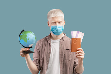 Tourism during coronavirus pandemic. Albino guy in protective mask holding globe, passport and plane tickets
