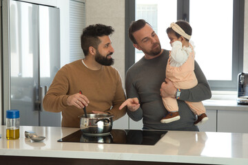Gay married couple cooking with their daughter in the kitchen of their home.