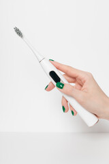 Female hand with manicure holds a white electric toothbrush