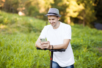 Young man in hat use mobile phone, book online rental electric scooter in city. Innovative transport