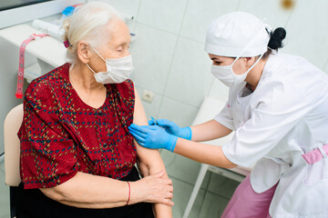 a nurse wearing a medical mask and rubber gloves is injecting or injecting a vaccine against the virus into the shoulder of an elderly woman . Vaccination and prevention of coronavirus infection.