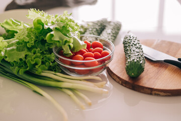 Healthy foods are on the table in the kitchen. Salad, cucumbers, tomatoes and a knife. Cooking at home