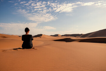 Fototapeta na wymiar A woman is sitting on the golden sand dune of the Namib desert.