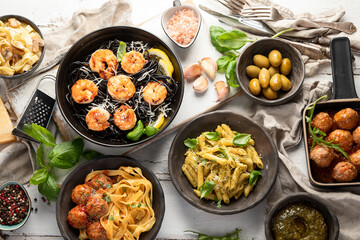 Assortment of Italian pasta with traditional snacks and sauces for dinner on white wooden background.