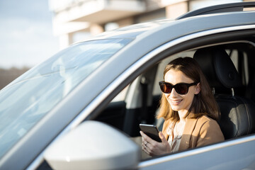 Young woman in sunglasses talking on the phone and driving a car. Businesswoman going to work from the house.