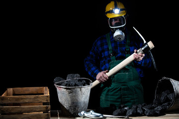 A miner with a protective helmet on and a flashlight and dust mask in his hands holds a mining cliff