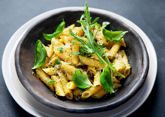Pasta spaghetti with homemade pesto and fresh basil leaves on dark background. Italian cuisine concept.