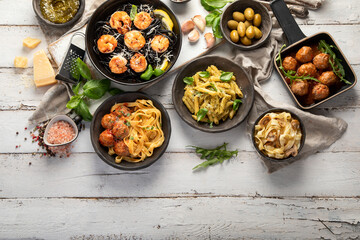 Assortment of Italian pasta with traditional snacks and sauces for dinner on white wooden background.