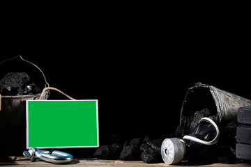 Black charcoal lies on a wooden platform and in a bucket with a green placard posted to be filled....