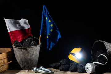On a wooden platform stands a bucket of coal with European Union and Polish flags stuck in it. Dust...