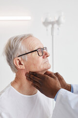 Unrecognizable African-American doctor palpating neck of senior man during examination in hospital room, side view