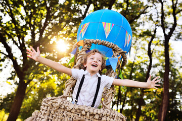 a child a small boy with curly hair in a basket of a blue balloon smiles and looks into the...