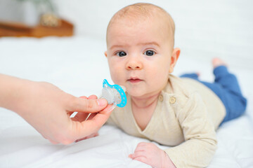 hand gives a pacifier to her baby son on a white background.