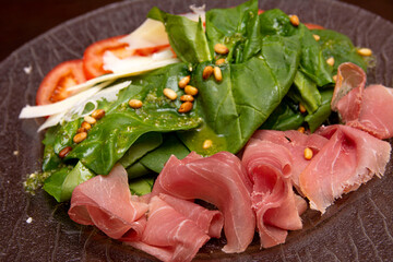 Salad of prosciutto, green spinach and fresh tomatoes, sprinkled with pine nuts.