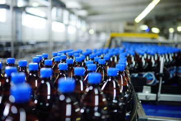 A lot of yellow plastic PET bottles with blue lids with drinks or beer on the conveyor belt on the background of the brewery.