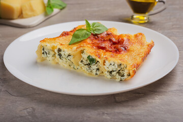 Traditional Cannelloni with ricotta and spinach- close up on white dish on stone table. Italian pasta. Mediterranean cuisine.