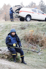 Men work in emergencies. Emergency workers work outdoors. A man in uniform works with a metal detector