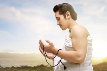 Asian Muslim man in ihram clothes praying with prayer beads on his hands