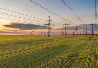 high voltage lines and power pylons in a green agricultural field against a saturated sunset sky