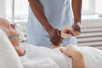 Obraz na płótnie Canvas Close up of African-American male nurse holding hand of senior man in hospital and comforting him, copy space